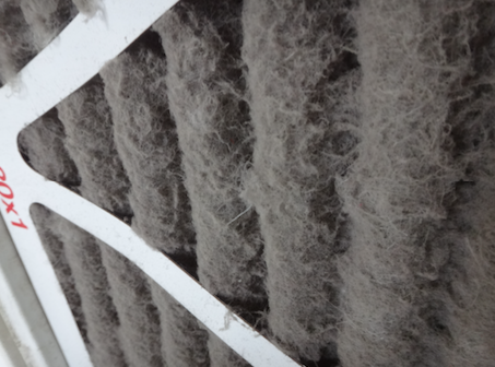 A dirty, pleated HVAC air filter (likely with a MERV rating between 5 and 13), shown with trapped lint, dust, and other airborne contaminants.