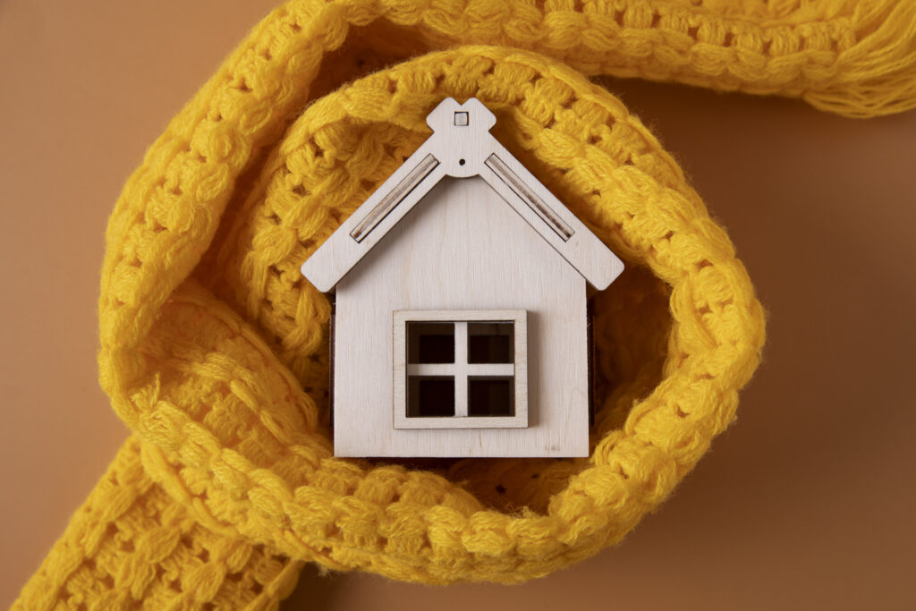 Small wooden toy house encircled by bright yellow knit scarf—symbolizing the warmth of a home heating system.