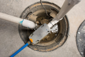 A sump pump installed in a circular basement pit with connected PVC pipes and an electrical box, surrounded by a concrete floor.