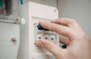 A hand is flipping a switch on an electrical circuit breaker panel.