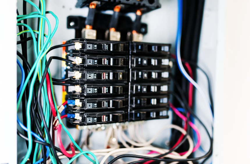 Close-up of an open electrical panel with multiple circuit breakers and various colored wires connected.