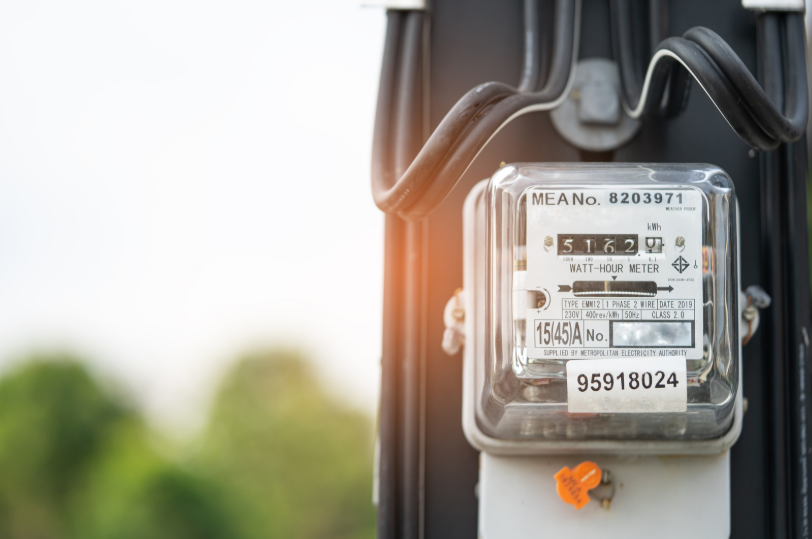 Close-up of an analog electricity meter attached to a pole, displaying numbers and various identification labels, with blurred greenery in the background.