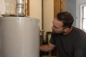 %Focuskw% | Precision Plumbing &Amp; Heating A man inspects a water heater in a utility room, looking closely at the tank and its fittings.