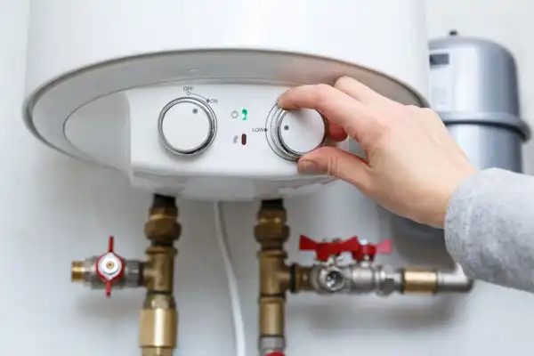 Hand adjusting the temperature dial on a wall-mounted tank
