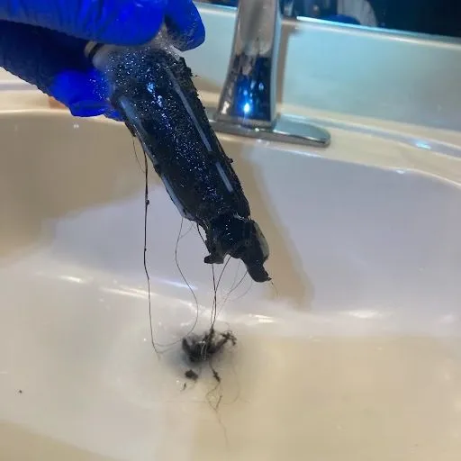 a gloved hand holding a bathroom sink drain plug with build up and hair on it