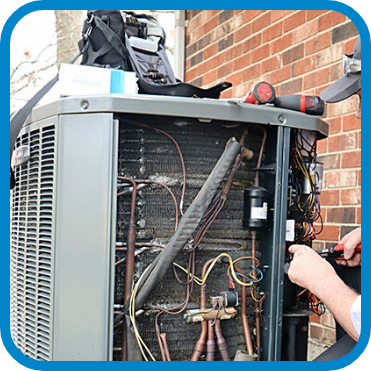 A technician repairing an outdoor HVAC unit, surrounded by tools and wiring. The unit is open, revealing internal components like coils and pipes.